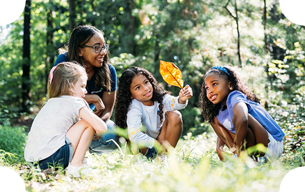 Three girls and their leader in a meadow looking at a leaf